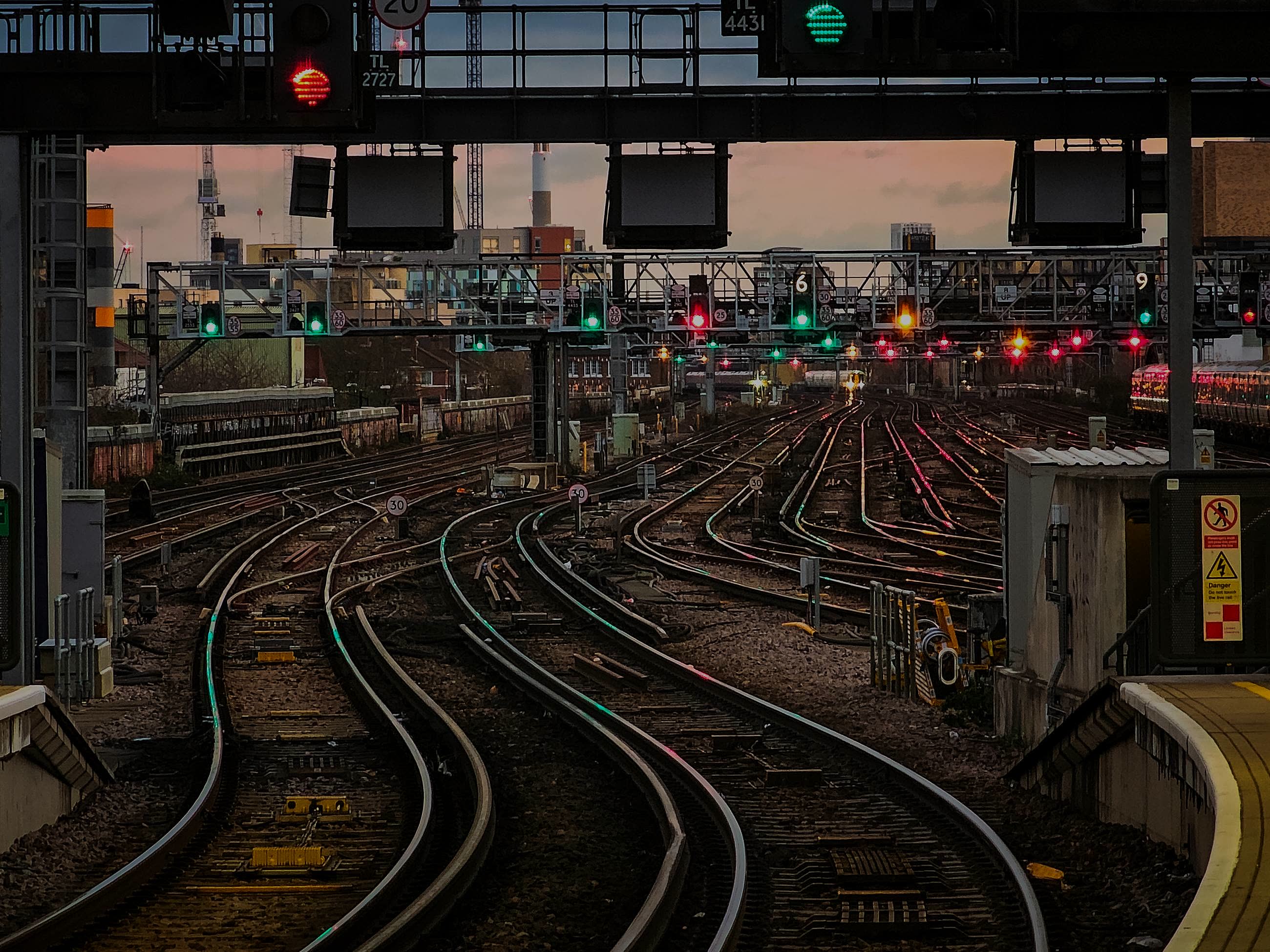 A rail yard at dusk, tracks fanning out under signal gantries.