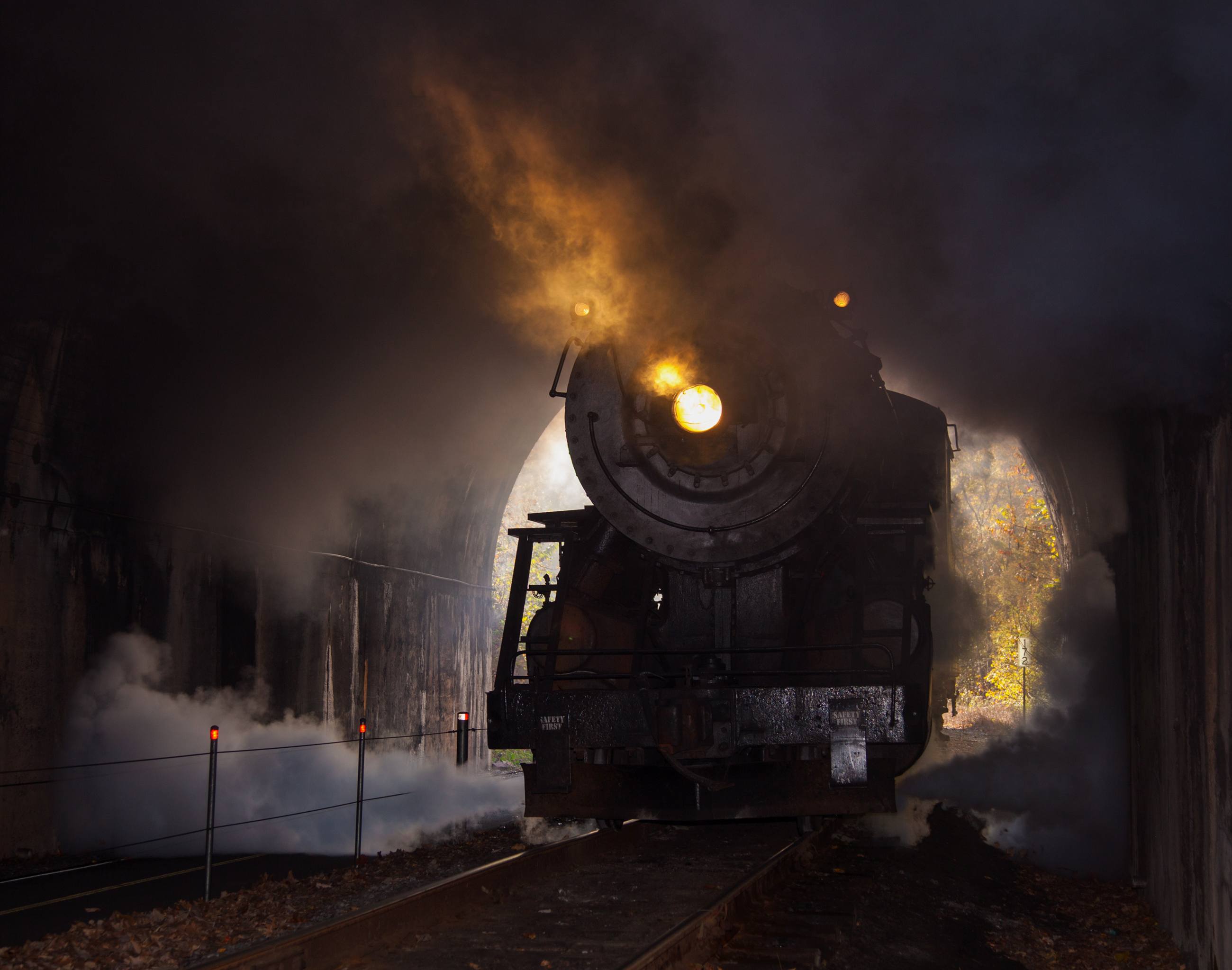 A steam locomotive emerging from a tunnel mouth wreathed in smoke.