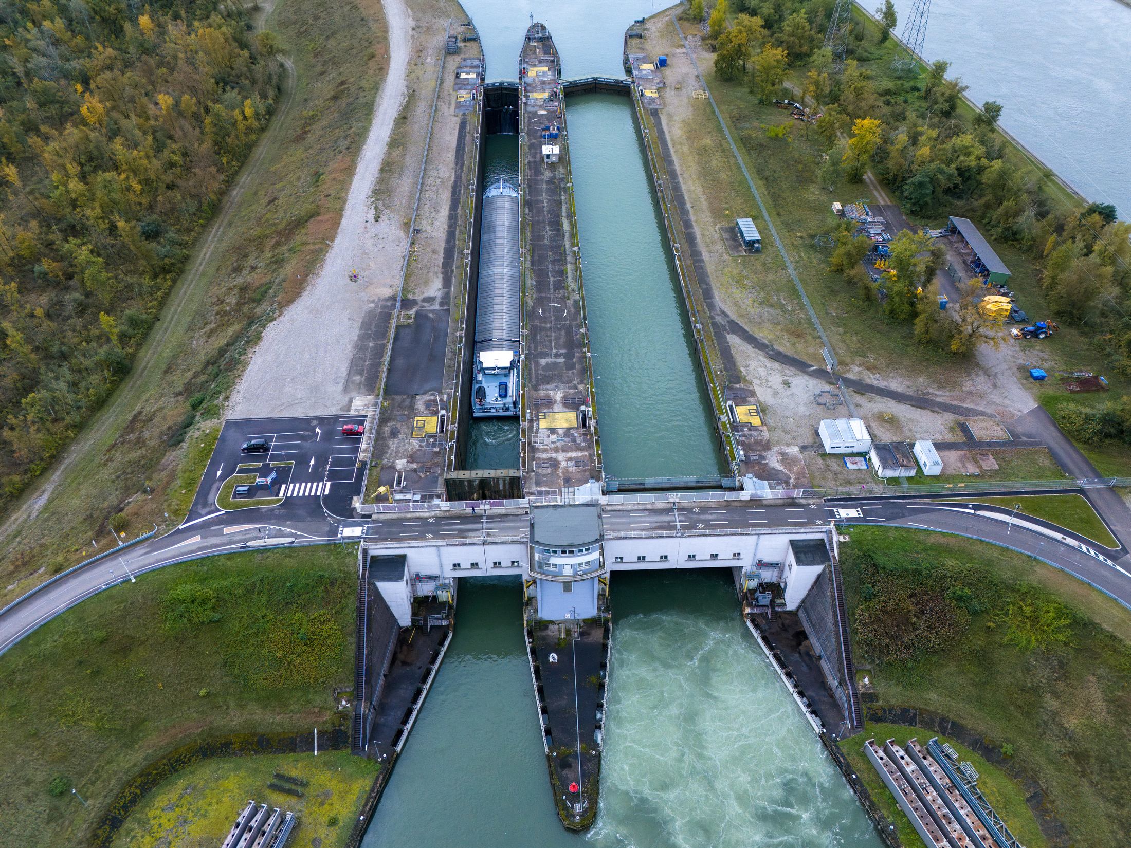 A river lock and weir seen from above, a barge held in the chamber while water pours through the gates below.