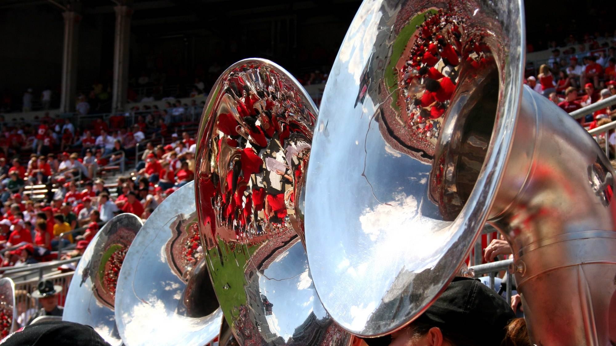 Sousaphone bells in a stadium, a crowd reflected and distorted across the polished brass.