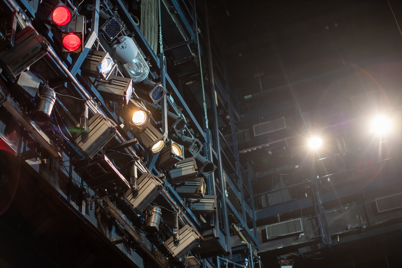 Stage lighting fixtures in red, white and amber converging on wire mesh catwalk rigging.