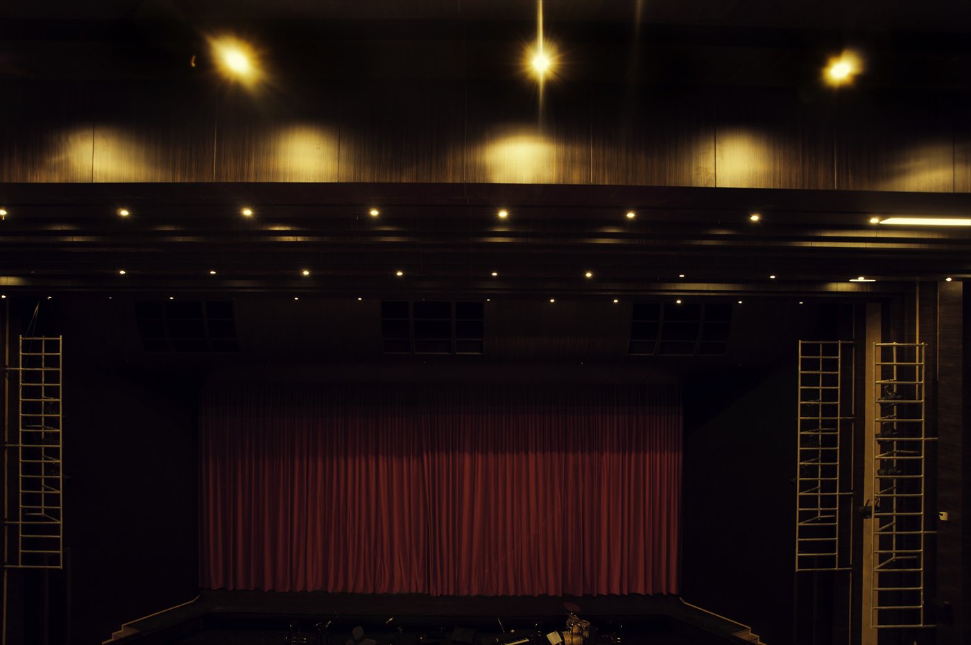 A closed red velvet curtain flanked by two ladders, equipment cases at the base of the frame.