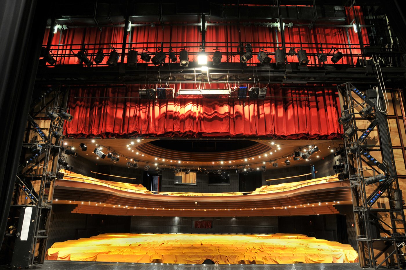 A view from the stage toward tiered seating, the stage floor and every row still covered in protective gold fabric, not yet unveiled.