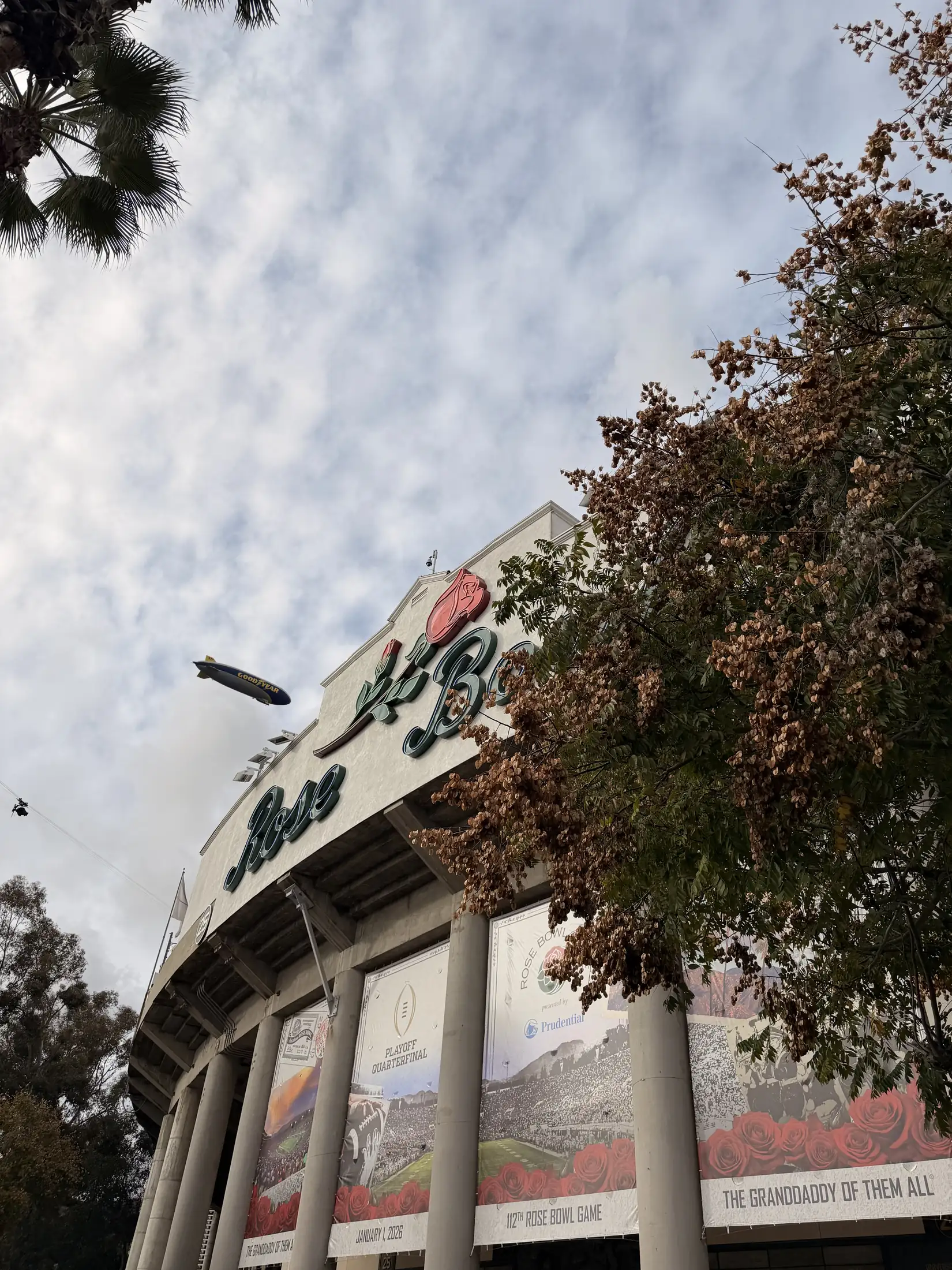 The Rose Bowl facade in Pasadena beneath a winter sky, with the Goodyear blimp overhead.